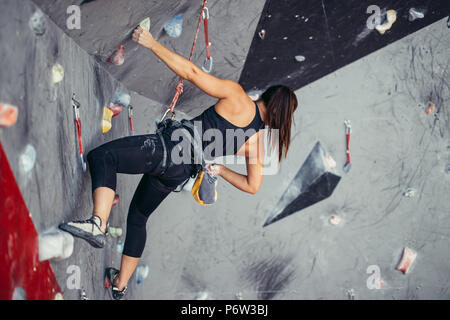 Extreme sport, stress relief, bouldering, people and healthy lifestyle concept. Young sporty muscular woman climbing up on top of rock wall in gym, lo Stock Photo