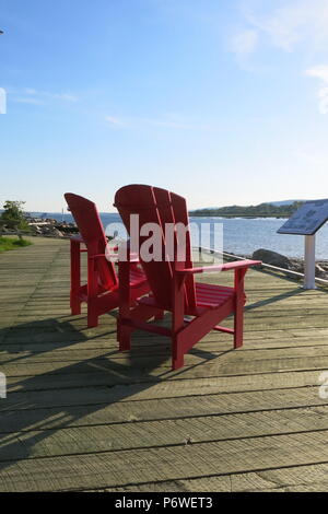 Two red adirondack chairs sit facing the lake and Rocky mountains