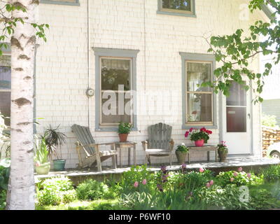 Two plastic Adirondack chairs on a summer patio outside a 