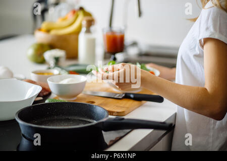 Cropped view of woman hands over black frying anti-stick pan on glass ceramic stove in focus. Kitchen utensils. Preparing food. Stock Photo
