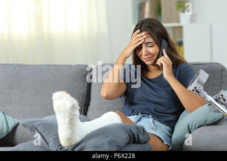 Sad disabled woman talking on phone sitting on a couch in the living room at home Stock Photo