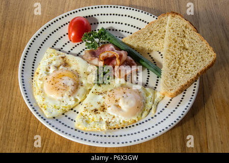 Eggs, bacon and tomato, garnished and set out on a plate with bread on the side Stock Photo