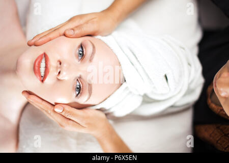 Top view, close-up of young woman getting face massage treatment at beauty spa salon. Lying at massage table ,looking at camera. Stock Photo