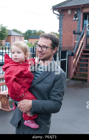 Baby girl wearing red puddle suit being held by her father Stock Photo