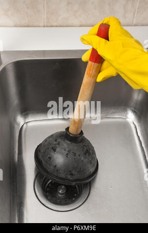 hand in glove using a plunger to cleaning a clogged sink Stock Photo