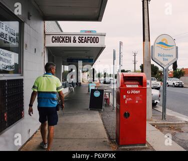 Post office and postman with fish and chips shop in the background at street in Seaview Downs, Adelaide Stock Photo