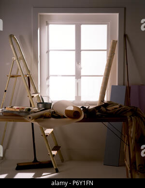 Rolls of wallpaper and decorating equipment and materials on a trestle table with a stepladder in a room before decoration Stock Photo