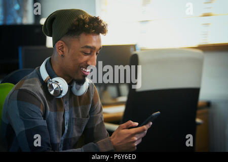 Smiling creative businessman with headphones using smart phone in office Stock Photo