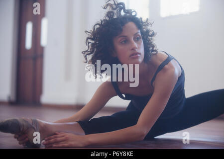 Focused young female dancer stretching leg in dance studio Stock Photo