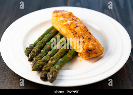 White plate with roasted salmon filet with fried asparagus on a dark wooden background Stock Photo