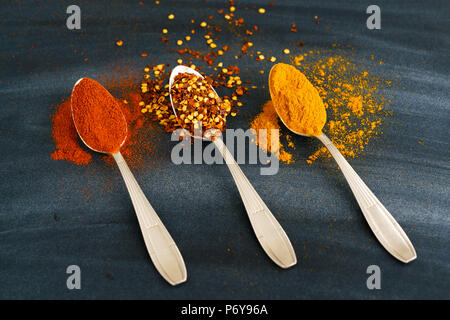 Vintage silver spoons full of paprika, turmeric and chili flakes on a dark background Stock Photo