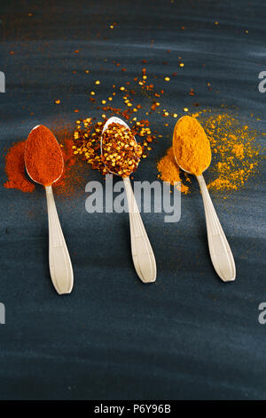 Vintage silver spoons full of paprika, turmeric and chili flakes on a dark background Stock Photo