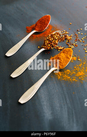 Vintage silver spoons full of paprika, turmeric and chili flakes on a dark background Stock Photo
