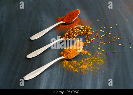 Vintage silver spoons full of paprika, turmeric and chili flakes on a dark background Stock Photo