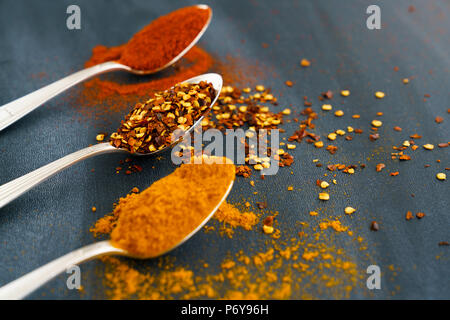 Vintage silver spoons full of paprika, turmeric and chili flakes on a dark background Stock Photo