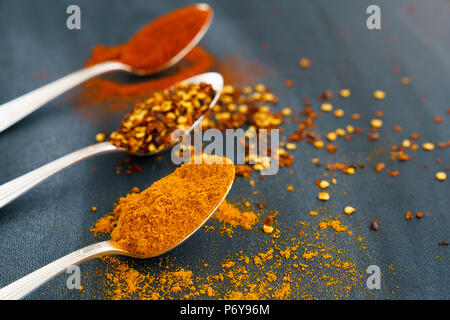 Vintage silver spoons full of paprika, turmeric and chili flakes on a dark background Stock Photo