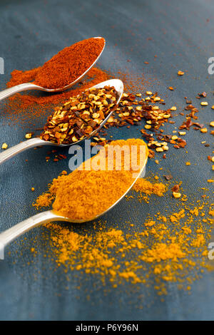 Vintage silver spoons full of paprika, turmeric and chili flakes on a dark background Stock Photo