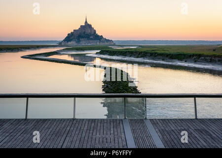 The Mont Saint-Michel tidal island at sunrise and high tide with the still waters of the Couesnon river and the wooden footbridge over the dam. Stock Photo