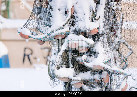 Hanging fishnets covered on snow in front of ship on cloudy winter day Stock Photo