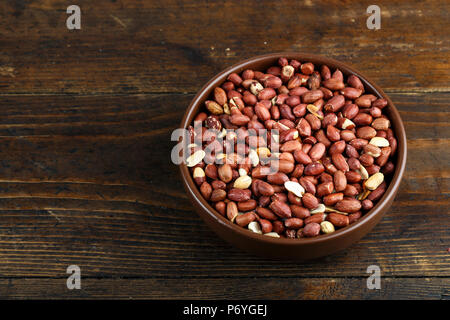 peanuts in a clay plate on a wooden background. place for text Stock Photo