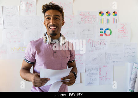 Portrait smiling, confident creative businessman hanging paperwork on office wall Stock Photo