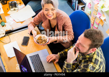 Creative business people eating cereal, working at laptop on office Stock Photo