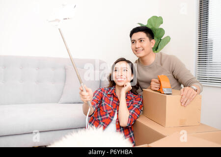 home, people, repair and real estate concept - smiling couple with big cardboard boxes moving to new place and taking smartphone selfie Stock Photo