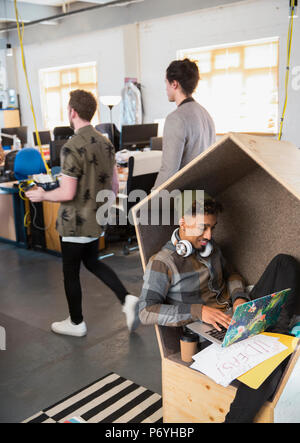 Creative businessman with headphones using laptop in office cubby Stock Photo