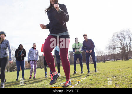 Team cheering woman doing speed ladder drill in sunny park Stock Photo