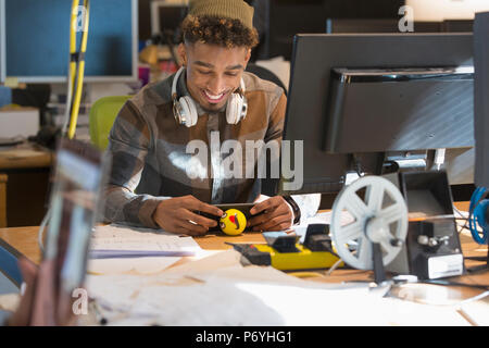 Smiling creative businessman with headphones using smart phone at computer in office Stock Photo