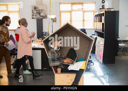 Creative businessman with headphones working at laptop in cubby Stock Photo