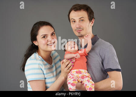 Young parents with small baby isolated on grey background Stock Photo