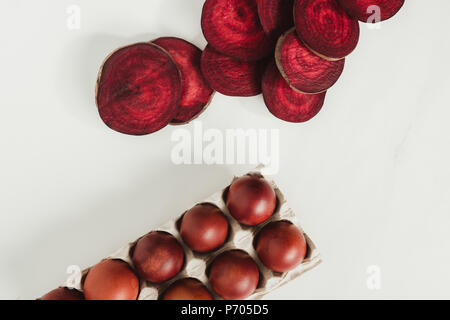 top view of painted chicken eggs in egg box and beetroot slices on grey Stock Photo