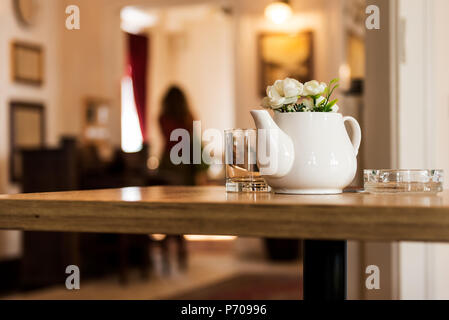 Indoor Restaurant Decoration with Ceramic Milk Pot with Flowers on a Wooden table with a gallery in the background Stock Photo