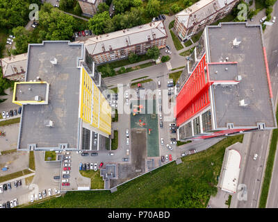 Aerial top view of two tall skyscrapers of red and yellow colors among small buildings with parking for cars and a children's playground in the yard w Stock Photo