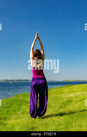 A yoga instructor demonstrates yoga poses during an outdoor yoga session in nature with blue skies and brilliant colours. Stock Photo