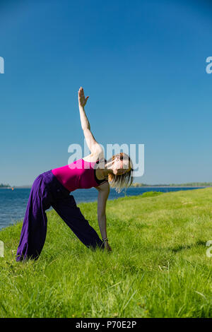 A yoga instructor demonstrates yoga poses during an outdoor yoga session in nature with blue skies and brilliant colours. Stock Photo