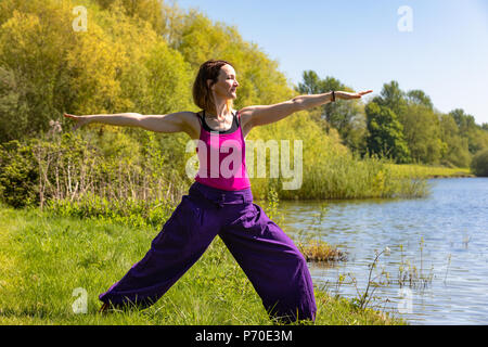 A yoga instructor demonstrates yoga poses during an outdoor yoga session in nature with blue skies and brilliant colours. Stock Photo