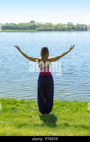 A yoga instructor demonstrates yoga poses during an outdoor yoga session in nature with blue skies and brilliant colours. Stock Photo