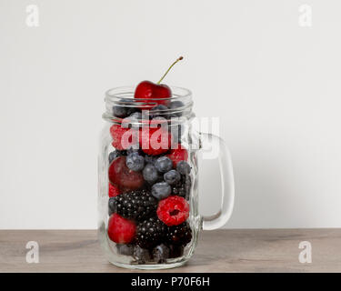 Abstract composition portraying blackberries, blueberries, raspberries and cherries in transparent glass mug on white background - healthy snack conce Stock Photo