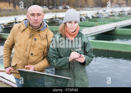 Portrait of confident male farmer with female worker near fish tanks on farm Stock Photo