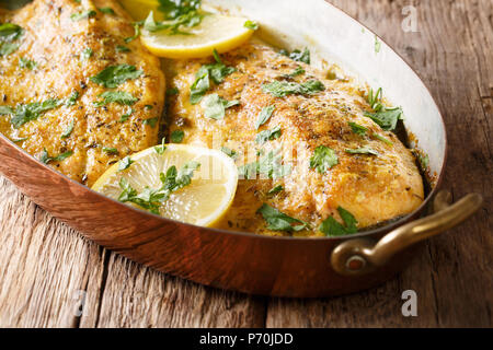 Baked trout fish with garlic lemon butter sauce, parsley closeup in a copper frying pan on a table. horizontal Stock Photo