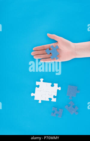 cropped image of businesswoman assembling puzzles and holding one piece on hand isolated on blue, business concept Stock Photo