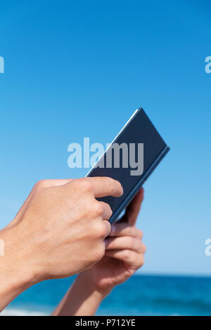 closeup of a young caucasian man reading a book on the beach, with some blank space on top Stock Photo