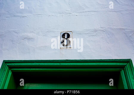 Ceramic black number eight, 8 outside on white painted wall over green wooden door Stock Photo