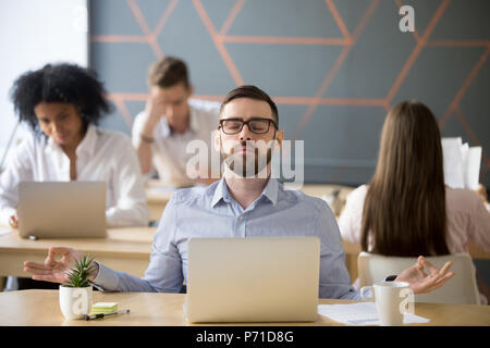 Calm male worker meditating in lotus position at workplace Stock Photo