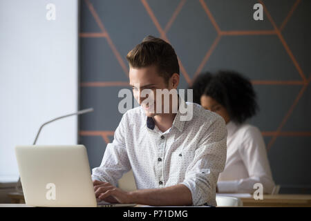 Happy millennial worker busy working at laptop in office Stock Photo