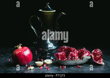 Black teapot and pomegranates with walnuts on concrete surface Stock Photo