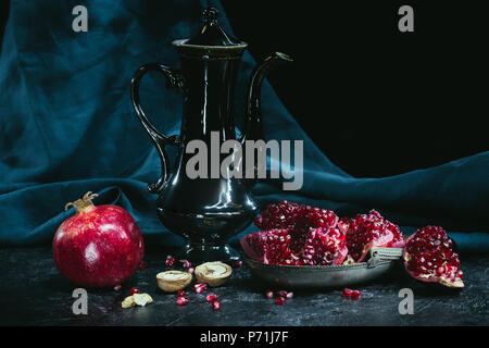 Black teapot and pomegranates on dark turquoise fabric Stock Photo