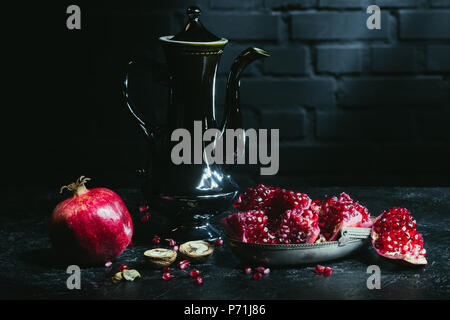Black teapot and pomegranates on concrete surface Stock Photo